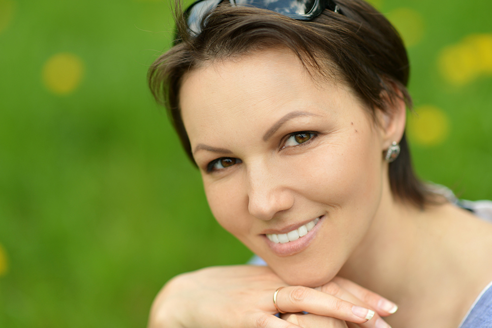 Mujer de aproximadamente 45 años sonriendo. Su cabello es corto y castaño. Tiene unos lentes de sol en la cabeza y usa aretes