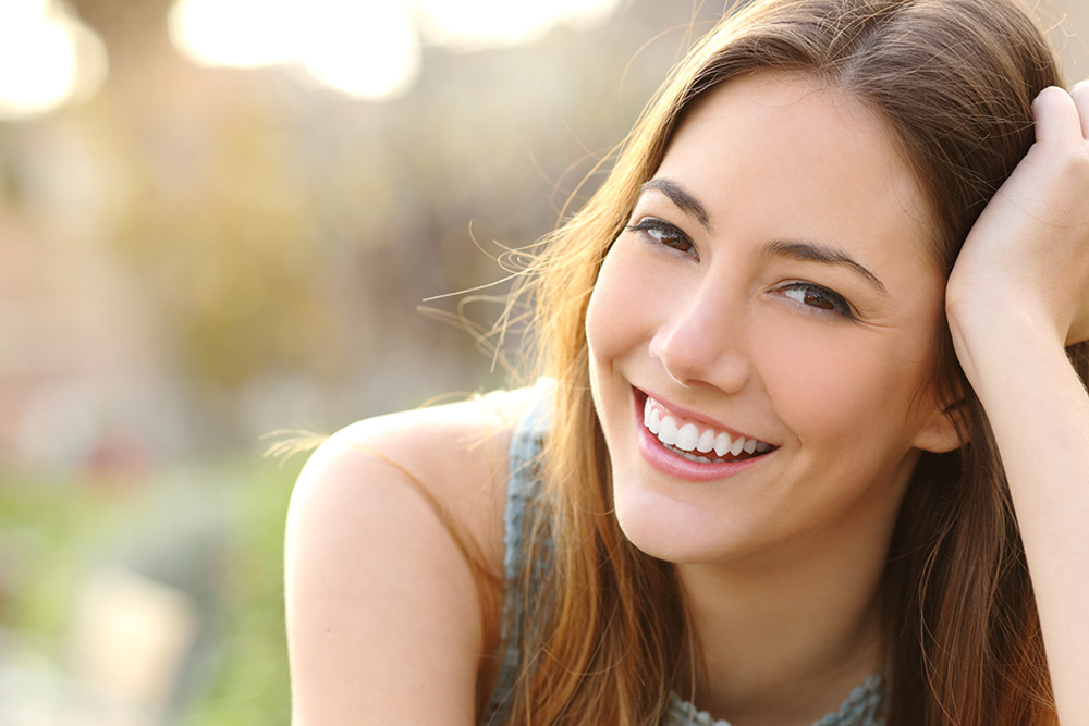 Mujer de aproximadamente 30 años riendo. Su cabello es castaño claro y largo. Está usando una blusa sin mangas de color gris