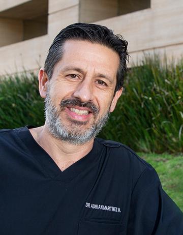 Es la foto de perfil de un coloproctólogo y cirujano general en la Ciudad de México, viste un uniforme negro de cuello V, es de tez apiñonada, usa bigote y su cabello es negro, está peinado hacia atrás. De fondo hay un pequeño jardín. Nuestro especialista brinda servicios en Hospital Angeles Acoxpa y en Clínica Londres  
