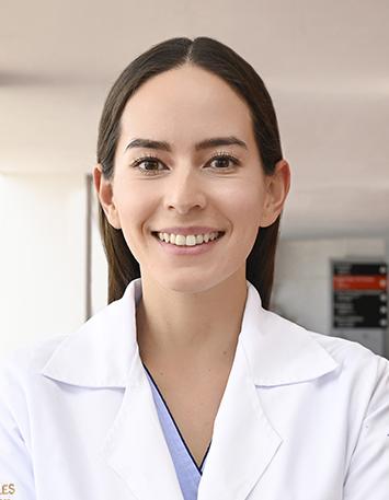 Es la foto de perfil de un nutriólogo en León de Hospital Angeles León. Utiliza una bata blanca, su cabello es lacio y castaño, la doctora está sonriendo y de fondo se encuentra en un consultorio.