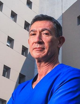 Es la foto de perfil de un dermatólogo en Huixquilucan. Tiene el cabello gris. Tiene los brazos cruzados y está serio. Usa un uniforme médico azul.