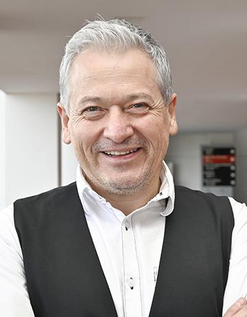 Es la foto de perfil de un dermatólogo pediátrico en León de Hospital Angeles León. Usa camisa blanca con un chaleco negro, el doctor es canoso y está sonriendo.
