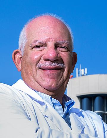 Es la foto de perfil de un ginecólogo y obstetra en Huixquilucan de Hospital Angeles Lomas. Utiliza una bata blanca con una camisa azul, tiene el cabello canoso y está sonriendo.