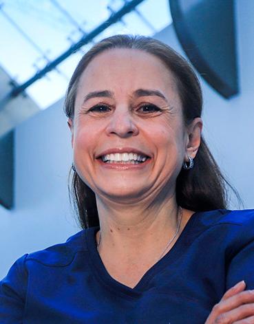 Es la foto de perfil de una dermatóloga en Huixquilucan de Hospital Angeles Lomas. Usa un uniforme azul, está sonriendo, tiene el cabello semirecogido y utiliza arracadas.