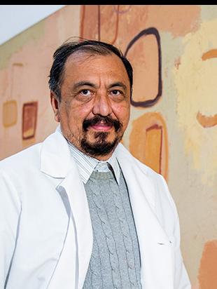 Es la foto de perfil de un cirujano cardiotorácico en Ciudad de México de Hospital Angeles Lindavista. Tiene el cabello, barba y bigote negro. Usa una bata blanca, un sueter gris y una camisa azul claro.