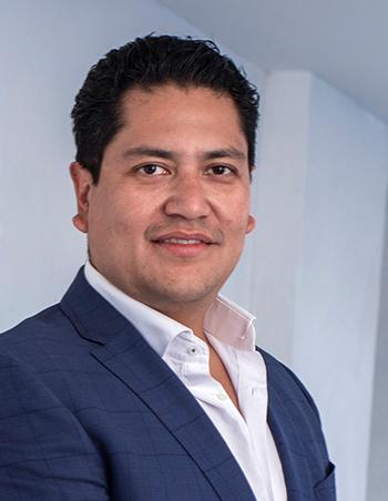 Es la foto de perfil de un cirujano general en Ciudad de México de Hospital Angeles. El doctor viste un traje azul marino y una camisa blanca, tiene el cabello rizado y está sonriendo.