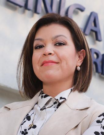 Es la foto de perfil de una ginecóloga y obstetra en Ciudad de México de Hospital Angeles Clínica Londres. La doctora tiene el cabello castaño y corto, con una expresión confiada. Viste una blusa con un diseño de flores en blanco y negro y un chaleco beige. Lleva aretes discretos y tiene una ligera sonrisa. El fondo muestra un edificio del hospital con un letrero en letras grandes.