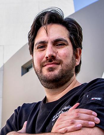 Es la foto de perfil de un nefrólogo en Huixquilucan de Hospital Angeles Lomas. Usa un uniforme negro, tiene los brazos cruzados, el cabello castaño, barba y bigote.