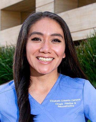 Es la foto de perfil de una cirujana plástica en Ciudad de México de Hospital Angeles. La doctora tiene un uniforme azul cielo, está sonriendo, su cabello es negro y largo. 