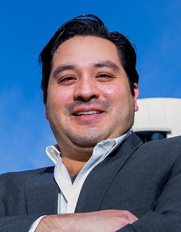 Es la foto de perfil de un ortopedista y traumatólogo en Huixquilucan de Hospital Angeles Lomas. Usa un saco negro, una camisa blanca, tiene los brazos cruzados y está sonriendo.