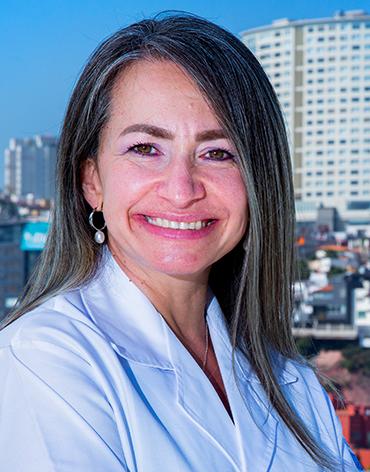 Es la foto de perfil de una anestesióloga en Huixquilucan de Hospital Angeles Lomas. Usa una bata blanca, está sonriendo, tiene cabello lacio y luces rubias.