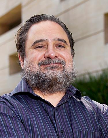 Es la foto de perfil de un ortopedista y traumatólogo en Ciudad de México de Hospital Angeles. El doctor tiene una camisa negra con franjas en color azul claro y morado oscuro, las líneas son verticales. El doctor tiene una barba canosa y larga, está sonriendo.