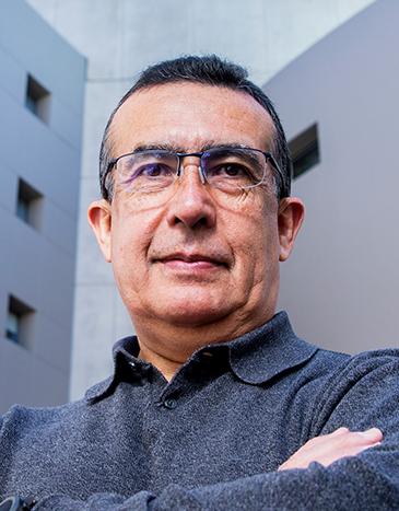 Es la foto de perfil de un cirujano neurológico en Huixquilucan de Hospital Angeles Lomas. Usa una camisa de color gris oscuro, tiene lentes, los brazos cruzados.