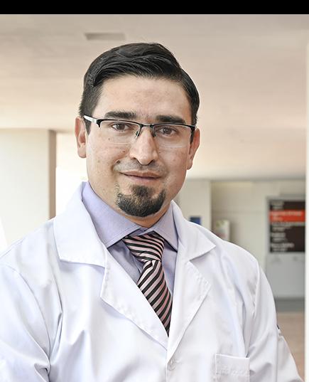 Es la foto de perfil de un cirujano oncológico en León de Hospital Angeles León. Utiliza una bata blanca con camisa y una corbata, tiene lentes, barba y está sonriendo.