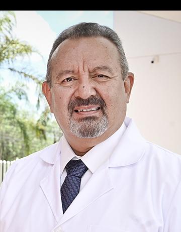 Es la foto de perfil de un cirujano general en León de Hospital Angeles León. Usa una bata blanca con camisa blanca y corbata oscura. Tiene el cabello canoso, barba y bigote.