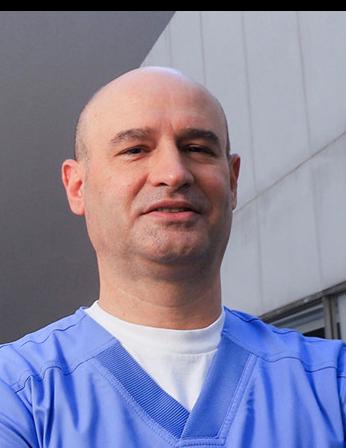 Es la foto de perfil de un otorrinolaringólogo en Huixquilucan de Hospital Angeles Lomas. Usa un uniforme azul, tiene una playera blanca debajo del uniforme y está sonriendo.