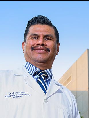 Es la foto de perfil de un pediatra especialista en cardiología pediátrica en Huixquilucan de Hospital Angeles Lomas. Usa una bata blanca, tiene camisa azul con rayas blancas y está sonriendo. 