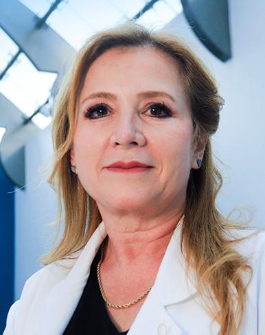 Es la foto de perfil de una cirujana plástica en Huixquilucan de Hospital Angeles Lomas. La doctora usa una bata blanca negra, tiene una blusa negra, cabello rubio y largo.