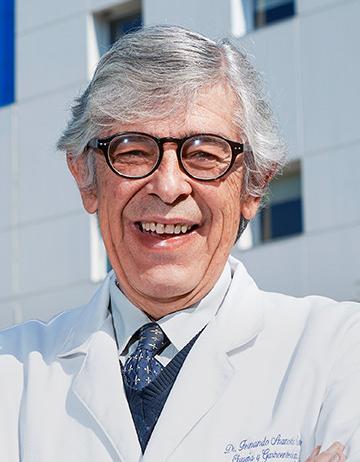 Es la foto de perfil de un cirujano general en Ciudad de México de Hospital Angeles Lindavista. Tiene el cabello gris. Usa lentes, bata blanca, suéter, corbata y camisa azul.