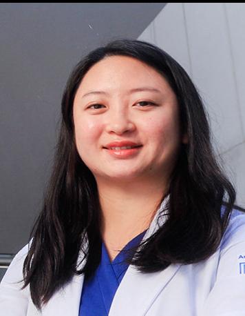 Es la foto de perfil de una gastrocirujana especialista en cirugía general en Ciudad de México de Hospital Angeles Clínica Londres. Utiliza una bata blanca con un uniforme médico azul debajo, tiene cabello negro debajo de los hombros y ojos rasgados. 