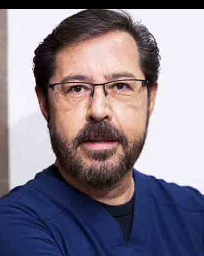 Es la foto de perfil de un especialista en coloproctología y cirujano general en Ciudad de México de Hospital Angeles Santa Mónica. Usa un uniforme médico azul. Tiene el cabello y barba negra. Usa lentes.