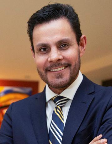 Es la foto de perfil de un cirujano oncológico en Ciudad de México de Hospital Angeles. Viste un traje azul marino con camisa blanca y corbata azul marino con tres líneas blancas y tres líneas amarillas.