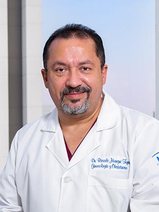 Es la foto de perfil de un ginecólogo y obstetra en Ciudad de México de Hospital Angeles Clínica Londres. Usa una bata blanca. Tiene el cabello negro y la barba negra con gris. Está sonriendo ligeramente.