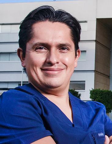 Es la foto de perfil de un ginecólogo y obstetra especialista en endoscopía en Ciudad de México de Hospital Angeles. Usa un uniforme de color azul con cuello V, tiene cabello oscuro y está sonriendo. 