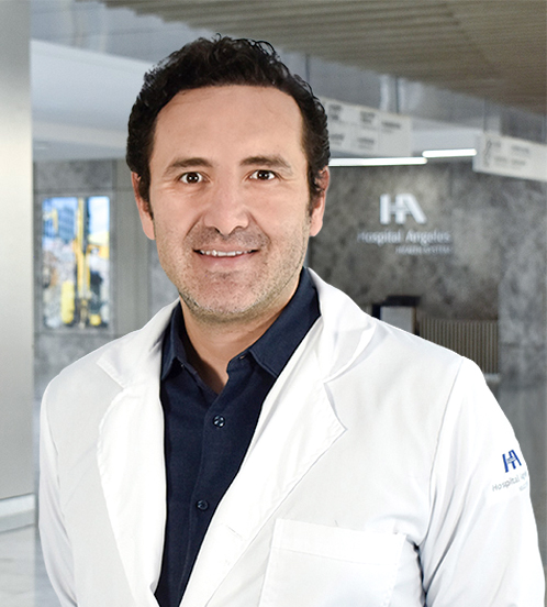 Es la foto de perfil de un ginecólogo y obstetra en Querétaro de Hospital Angeles Centro Sur. Usa una bata blanca con una camisa beige, es de tez blanca y cabello ondulado.