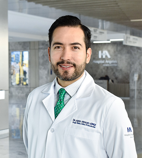 Es la foto de perfil de un cirujano plástico en Querétaro de Hospital Angeles Centro Sur. Usa una bata blanca con una camisa blanca y una corbata verde. Tiene el cabello y barba café.
