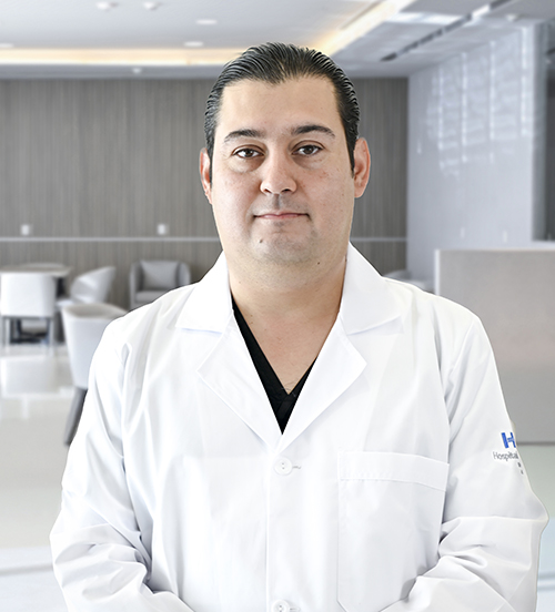 Es la foto de perfil de un cardiólogo y ecocardiografista en San Pedro Garza García de Hospital Angeles Valle Oriente. Usa una bata blanca con un uniforme médico color azul marino. Tiene el cabello café.