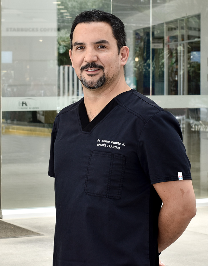 Es la foto de un cirujano plástico en Ciudad de México de Hospital Angeles. Utiliza un uniforme negro con su nombre bordado en letras blancas del lado izquierdo de su pecho y en brazo del mismo lado del mtiene bordado el logotipo del hospital. El fondo de la imagen es el frente del hospital.