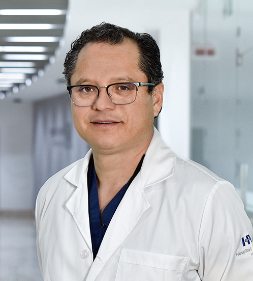 Es la foto de perfil de un cirujano cardiotorácico en Huixquilucan. Tiene el cabelo negro. Usa lentes, una bata blanca y un uniforme médico color azul.