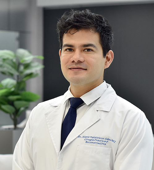 Es la foto de perfil de un cirujano plástico en Querétaro de Hospital Angeles Centro Sur. Usa una bata blanca con camisa blanca y corbata azul marino. Tiene el cabello oscuro y cejas pobladas.