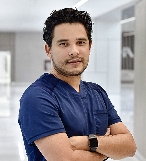 Es la foto de perfil de un ginecólogo y obstetra en Querétaro de Hospital Angeles Centro Sur. Usa un uniforme azul marino, es apiñonado, tiene los brazos cruzados y usa barba.