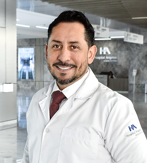 Es la foto de perfil de un ginecólogo y obstetra en Querétaro de Hospital Angeles Centro Sur. Usa una bata y camisa color blanco, con una corbata roja. Tiene el cabello color negro. Su barba y bigote es negro con algunas canas.
