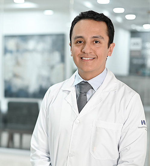 Es la foto de perfil de un cirujano neurólogo en Ciudad de México de Hospital Angeles Acoxpa. Usa una bata blanca con una camisa color azul claro y una corbata color gris. Tiene el cabello negro y está sonriendo.