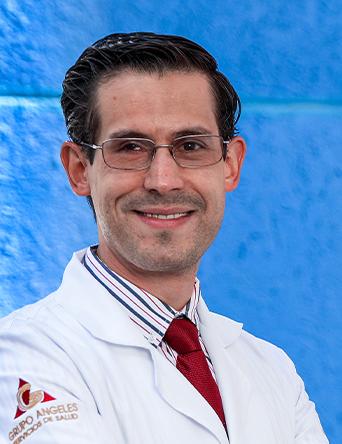 Es la foto de perfil de un nefrólogo en León de Hospital Angeles León. Viste una bata blanca con camisa blanca con rayas negras y una corbata roja. El fondo es azul.