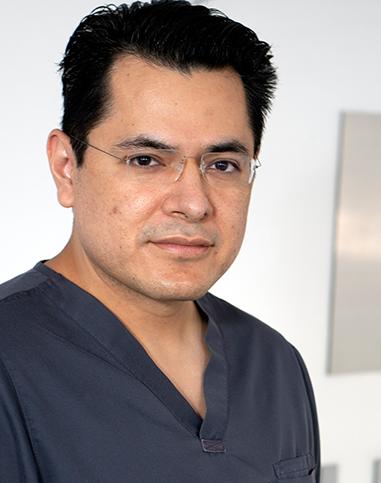 Es la foto de perfil de un cirujano plástico en Ciudad de México de Hospital Angeles Roma. Usa un uniforme médico azul oscuro. Tiene el cabello negro.