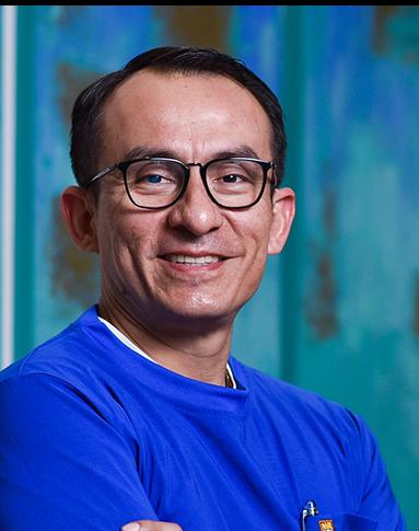 Es la foto de perfil de un ortopedista y traumatólogo en Villahermosa de Hospital Angeles Villahermosa. Usa un suéter azul . Tiene los brazos cruzados y usa lentes.