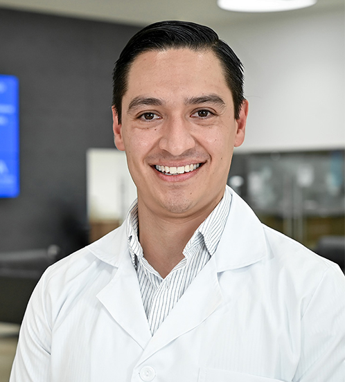 Es la foto de perfil de un ortopedista y traumatólogo en San Luis Potosí de Hospital Angeles San Luis Potosí.Usa una bata y camisa color blanco. Tiene el cabello negro. EStá sonriendo.