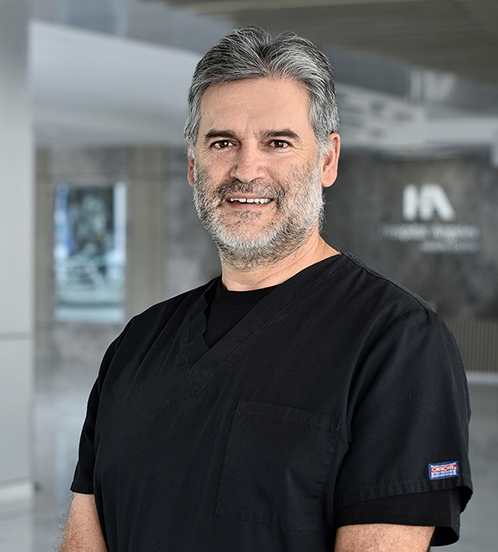 Es la foto de perfil de un cirujano general en Querétaro de Hospital Angeles Centro Sur. Tiene un uniforme negro, el cabello y la barba canosa y está sonriendo.