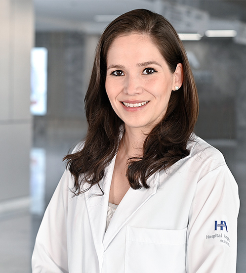 Es la foto de perfil de una cirujana general en Querétaro de Hospital Angeles Centro Sur. Usa una blusa azul y un collar dorado en forma del contorno de una mariposa. Tiene una coleta y está sonriendo.