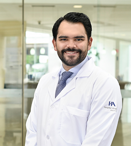 Es la foto de perfil de un internista en Ciudad de México de Hospital Angeles Acoxpa. Usa una bata de Hospital Angeles blanca. Tiene puesto una corbata color azul y una camisa blanca. Tiene el cabello y barba negro.