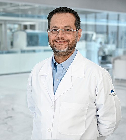 Es la foto de perfil de un patólogo en Guadalajara de Hospital Angeles Del Carmen. Utiliza un saco color azul y una camisa roja. Tiene lentes, el cabello corto  y está sonriendo.