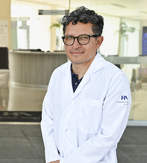 Es la foto de perfil de un ortopedista y traumatólogo en Ciudad de México de Hospital Angeles. El doctor tiene una bata de color blanca con una playera polo de color negro con el cuello gris. Tiene el cabello rizado, tez morena y viste unos lentes con el marco negro.