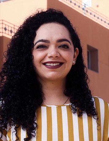 Es la foto de perfil de una ginecóloga y obstetra en Torreón de Hospital Angeles Torreón. Usa una blusa de rayas. Tiene el cabello largo, chino y negro.