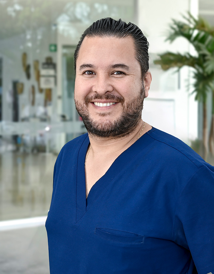 Es la foto de perfil de un ortopedista y traumatólogo en Ciudad de México de Hospital Angeles. El especialista tiene un uniforme azul marino, está sonriendo y tiene barba y bigote.
