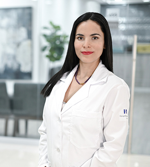 Es la foto de perfil de una radioterapeuta en Ciudad de México de Hospital Angeles Acoxpa. Usa una bata y blusa blanca. Tiene puesto un collar corto de color morado. Tiene el cabello color negro y lacio. Sus manos las tiene colocadas por debajo de su estómago.