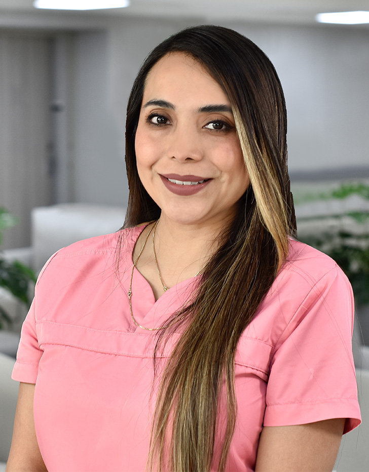 Es la foto de perfil de una otorrinolaringóloga en Ciudad de México de Hospital Angeles Metropolitano. Trae puesto un uniforme médico color rosa. Usa joyería color rosa. Tiene el cabello largo y lacio de color café con rayos güeros.